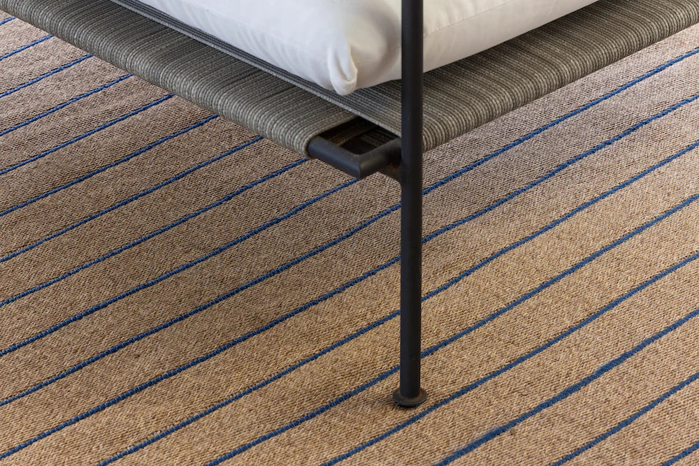 Close-up of a textured carpet with a chair leg on a striped patterned floor.