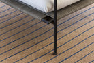 Close-up of a textured carpet with a chair leg on a striped patterned floor.