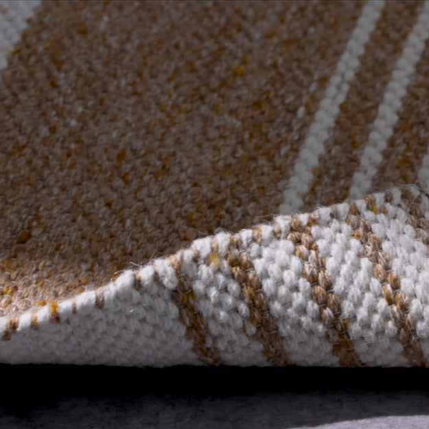 Close-up of a woven rug or textile showing a textured surface with diagonal stripes in tan, cream, and white, with one corner folded over to reveal the underside.