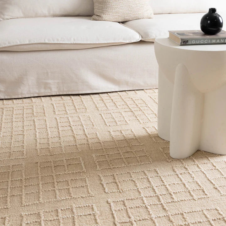 Beige patterned carpet in a living room setting with a sofa and coffee table.