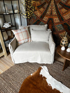 Gray armchair with plaid pillow in a room with patterned tapestry and wooden furniture.