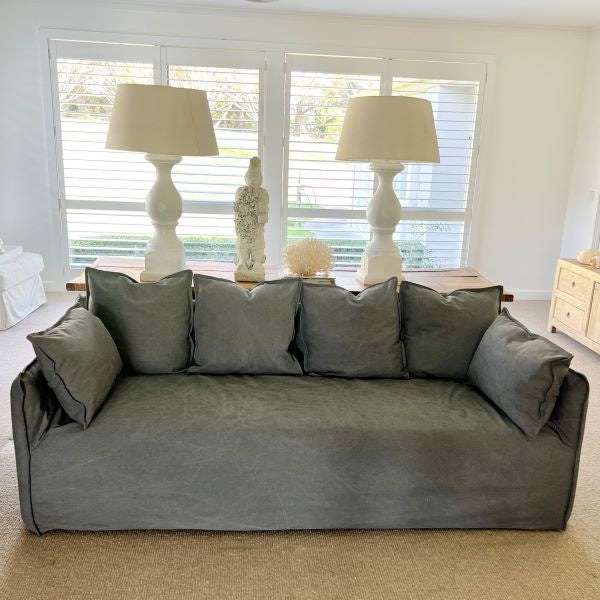 Gray sofa with cushions in a living room setting with lamps and decor.