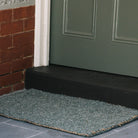 Green doormat in front of a green door on a brick wall background