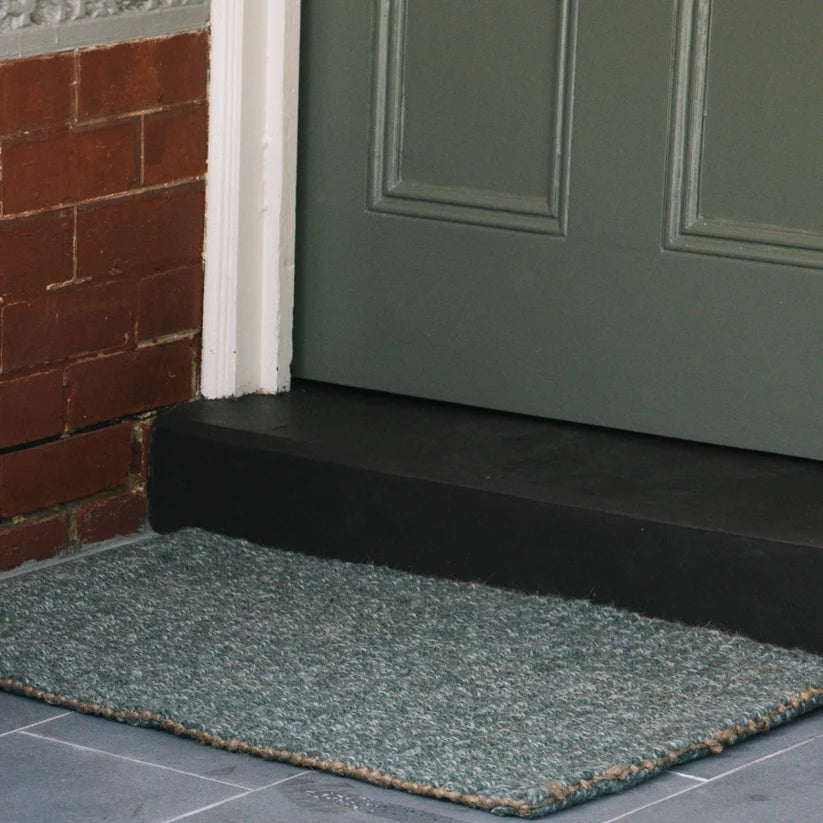 Green doormat in front of a green door on a brick wall background