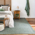 Cozy bedroom with a green rug, wooden nightstand, and bed with striped pillows.