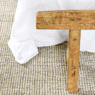 Wooden stool with a white cushion on a textured beige rug