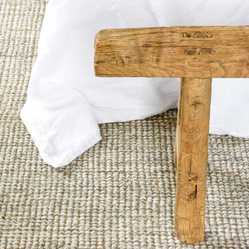 Wooden stool with a white cushion on a textured beige rug