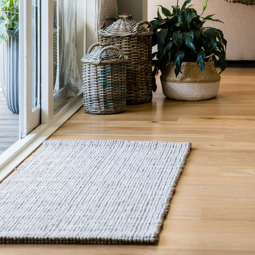 Rug on a wooden floor with baskets and plants in a room.