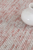 Close-up of a textured pink and beige carpet with a white ceramic vase.