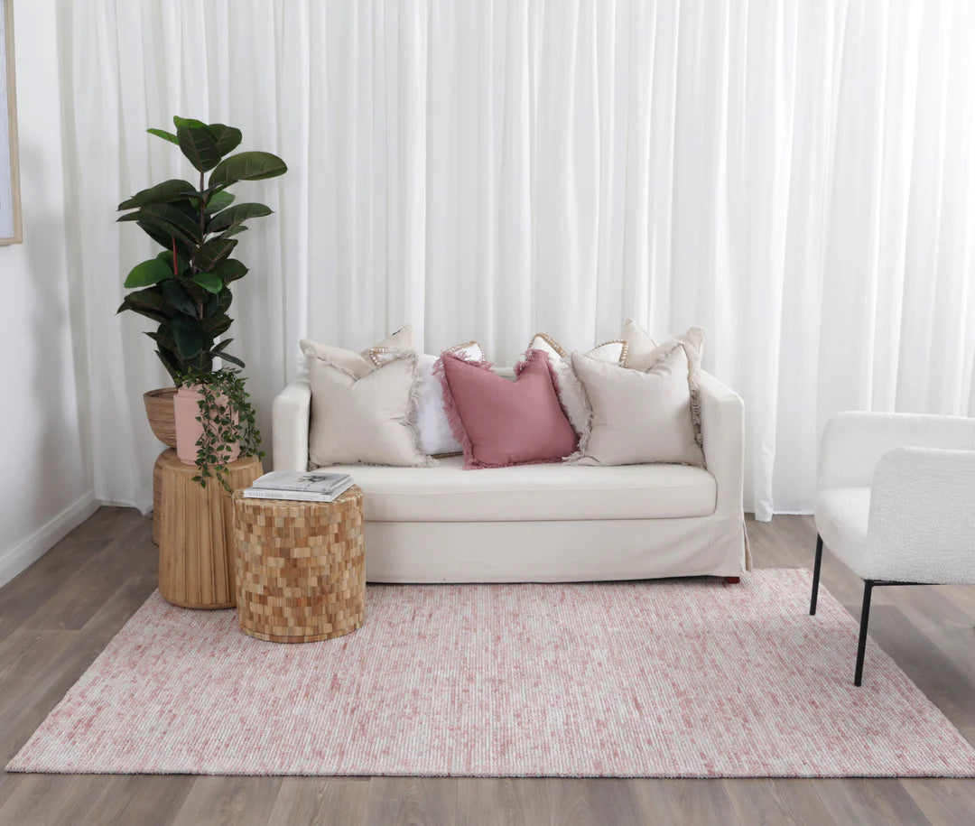 Living room with a beige sofa, pink cushions, and a plant on a wooden side table.