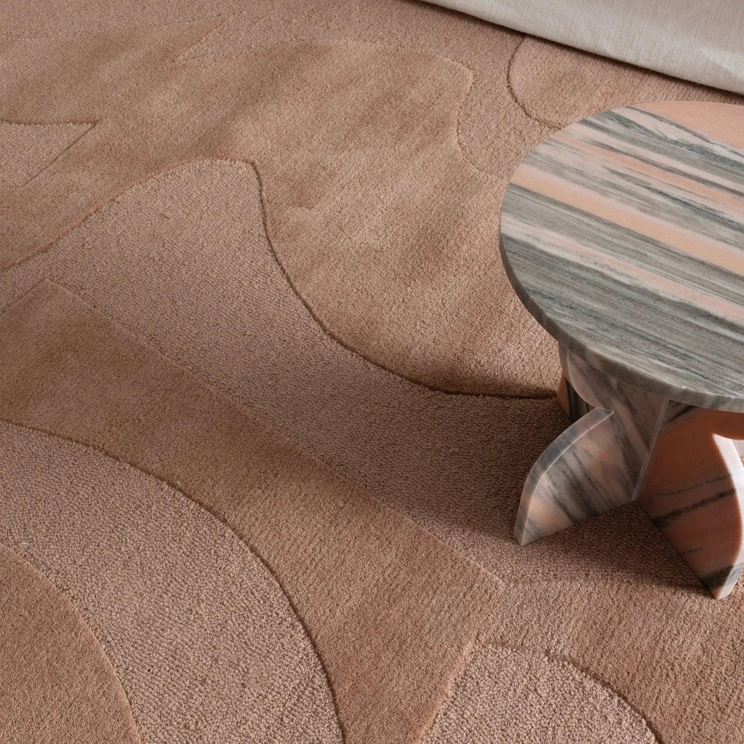 Close-up of a textured beige carpet with a small wooden stool featuring a marble pattern.