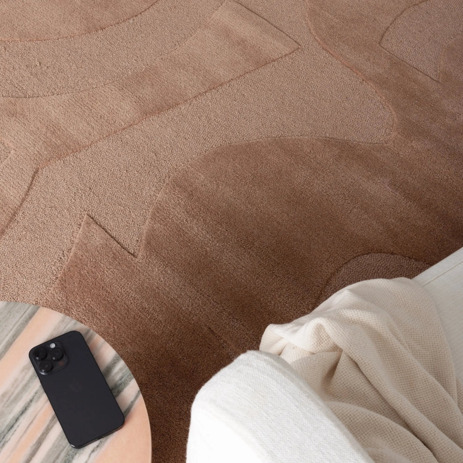 Person sitting on a brown textured rug with a phone beside them
