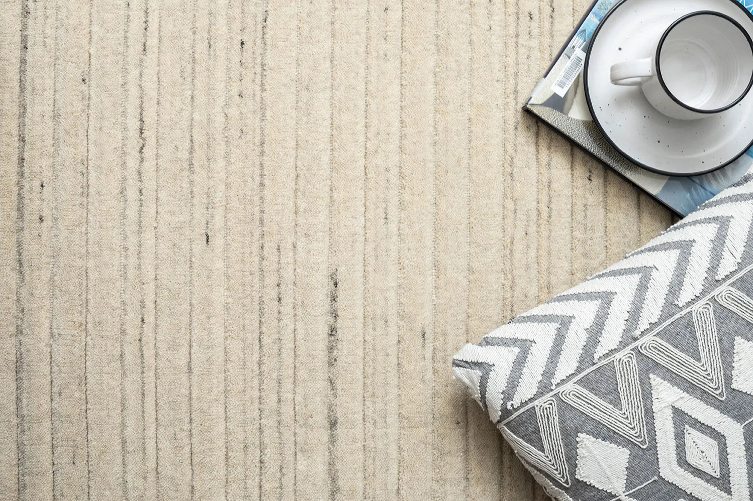 Textured beige surface with a geometric-patterned gray and white pillow and a small cup and saucer.