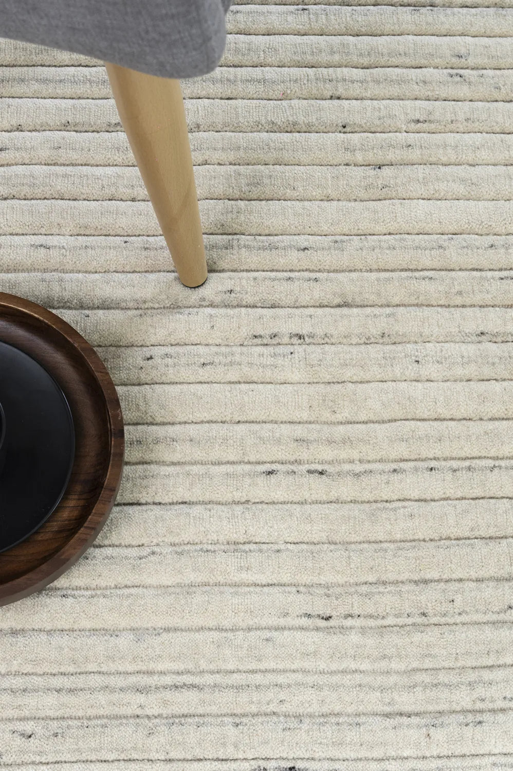 Close-up of a textured beige rug with a wooden chair leg and woven basket.