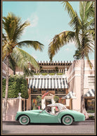A framed art print depicting a retro mint green convertible car parked on a street in front of a building with a black and white striped awning, framed by tall palm trees under a light blue sky.