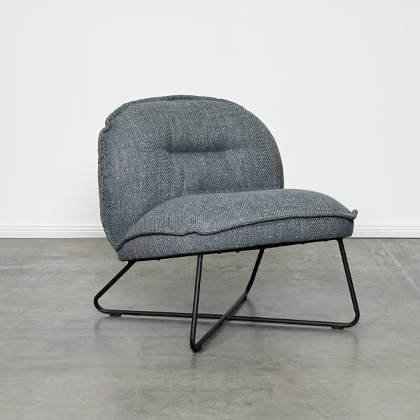 A modern lounge chair with a textured gray fabric cushioned seat and backrest, supported by a black metal frame, set against a plain white wall and gray concrete floor.