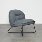 A modern low-profile accent chair upholstered in a textured gray fabric with a black metal frame, set against a minimalist white wall and gray concrete floor.