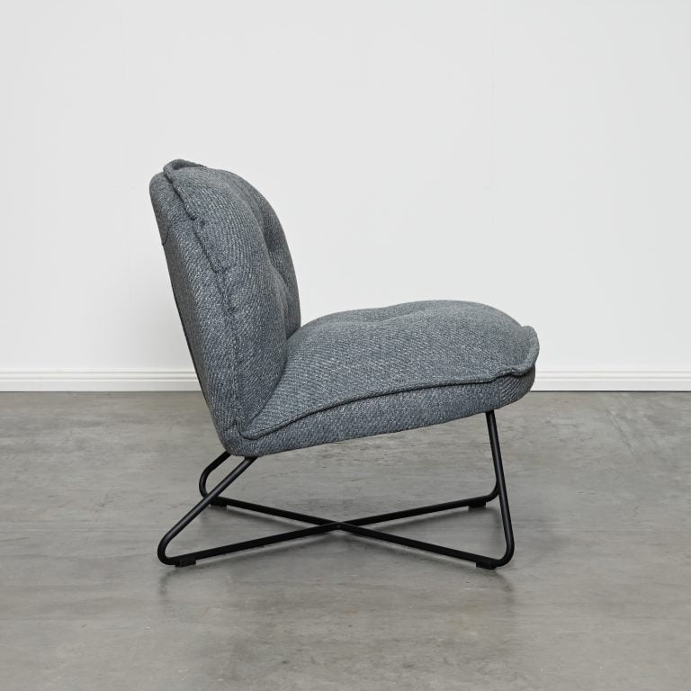 A modern gray upholstered accent chair with a black metal X-frame base, shown in profile against a white wall and concrete floor.