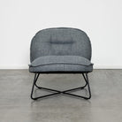 A modern gray upholstered accent chair with a black metal X-frame base, set against a minimalist white wall and concrete floor.