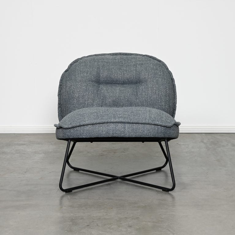 A modern gray upholstered accent chair with a black metal X-frame base, set against a minimalist white wall and concrete floor.