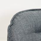 Close-up of a textured gray woven fabric, likely upholstery or a cushion, with a visible stitched edge against a plain light background.