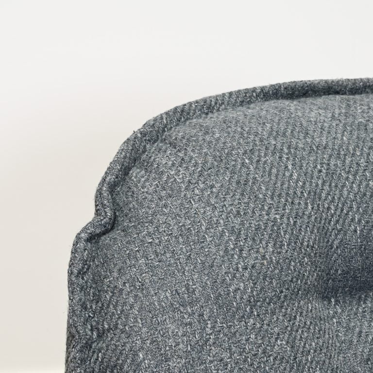 Close-up of a textured gray woven fabric, likely upholstery or a cushion, with a visible stitched edge against a plain light background.
