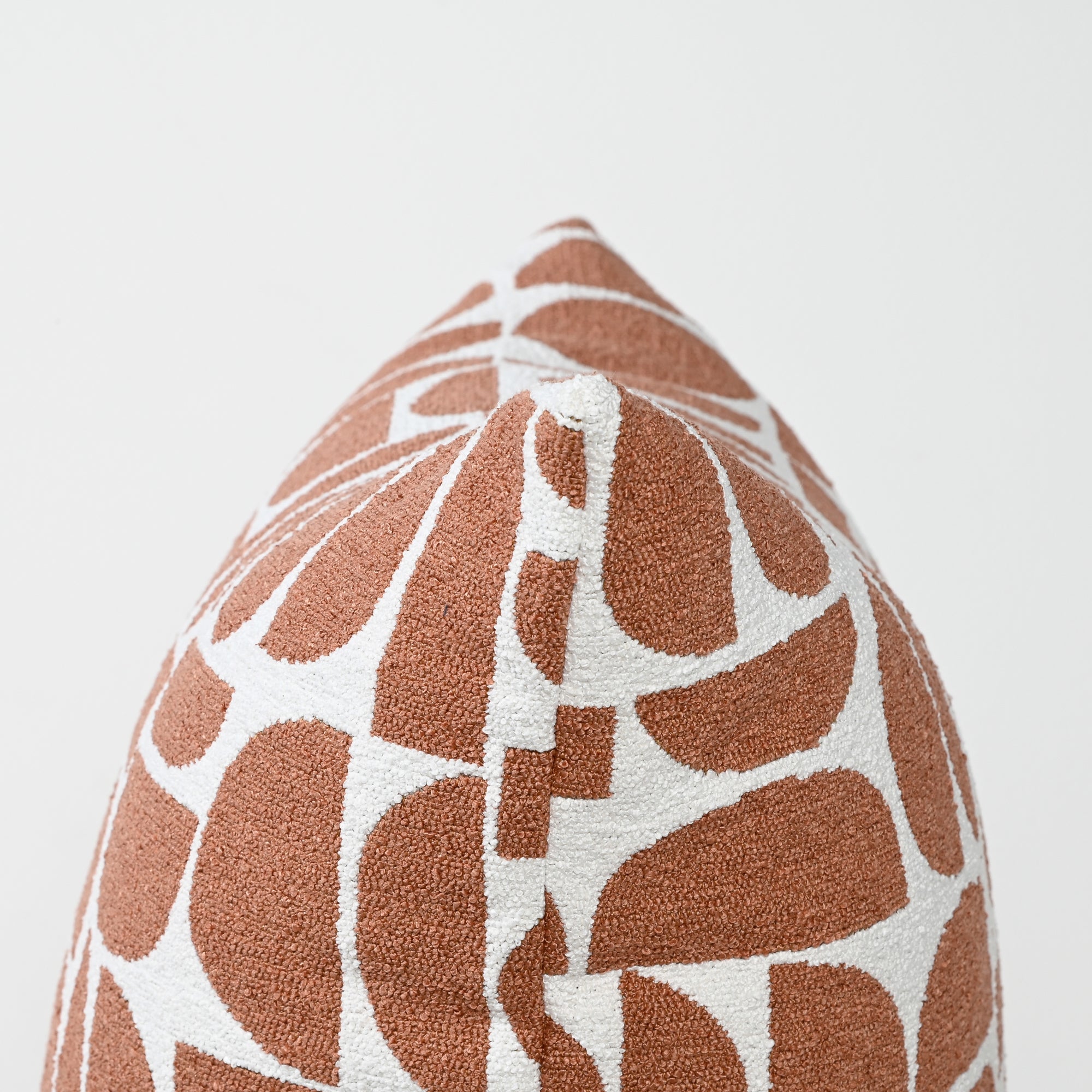 A close-up of a decorative throw pillow featuring a terracotta rust and white geometric pattern, shown against a plain light gray background.