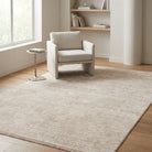 A large light beige area rug with a subtle textured pattern, shown in a bright, modern room with a white armchair, a small side table, and wooden flooring.