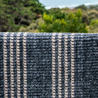Textured blue and beige rug with outdoor greenery in the background