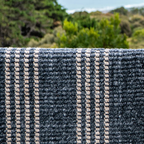 Textured blue and beige rug with outdoor greenery in the background