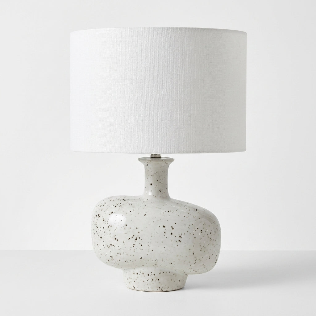 A table lamp with a textured white drum shade and a speckled ceramic base in off-white with black flecks, set against a plain white background.