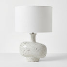 A table lamp with a textured white drum shade and a speckled ceramic base in off-white with black flecks, set against a plain white background.