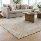 A large rectangular area rug in a neutral beige and cream textured pattern, shown in a bright, modern living room setting under a light beige sofa and a wooden coffee table.