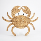 A decorative woven crab wall piece made from natural straw in a light tan color, featuring small black bead eyes, set against a plain white background.