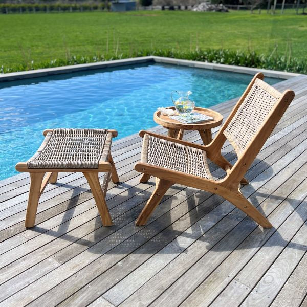 Wooden outdoor furniture set with a chair, ottoman, and small table by a pool.