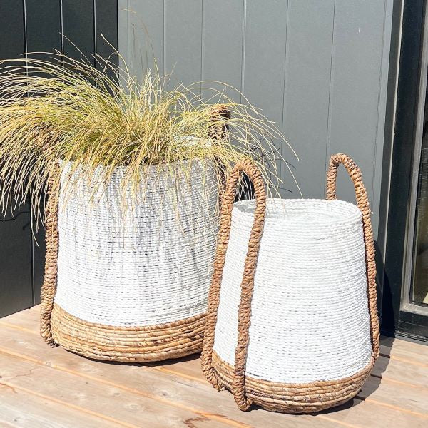 Two woven planters with grass on a wooden deck.