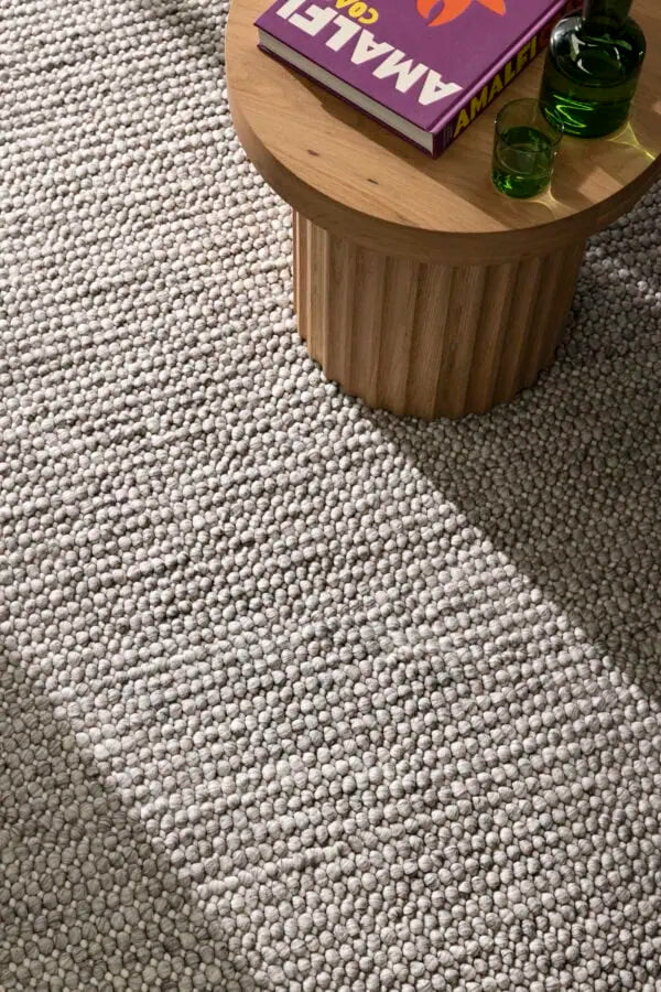 Small wooden table with a book and green glasses on a textured gray carpet
