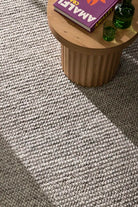 Small wooden table with a book and green glasses on a textured gray carpet