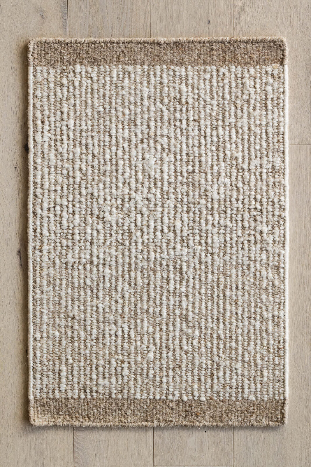 Textured area rug with a natural color palette on a wooden floor.