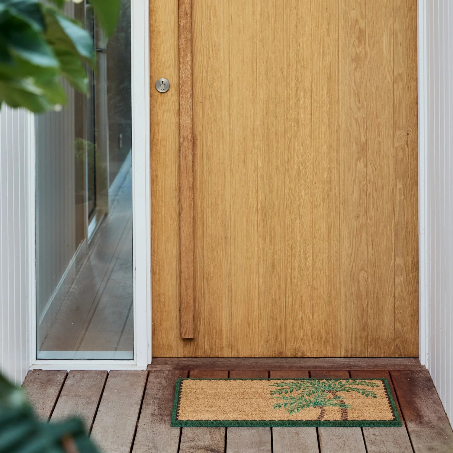 Palm tree door mat on timber decking in front of modern door way