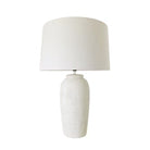 A table lamp with a textured white ceramic base and a matching white fabric drum shade, shown against a plain white background.