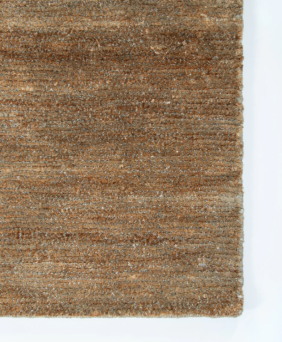 A close-up of a textured woven rug or fabric in earthy brown and tan tones, shown against a white background.