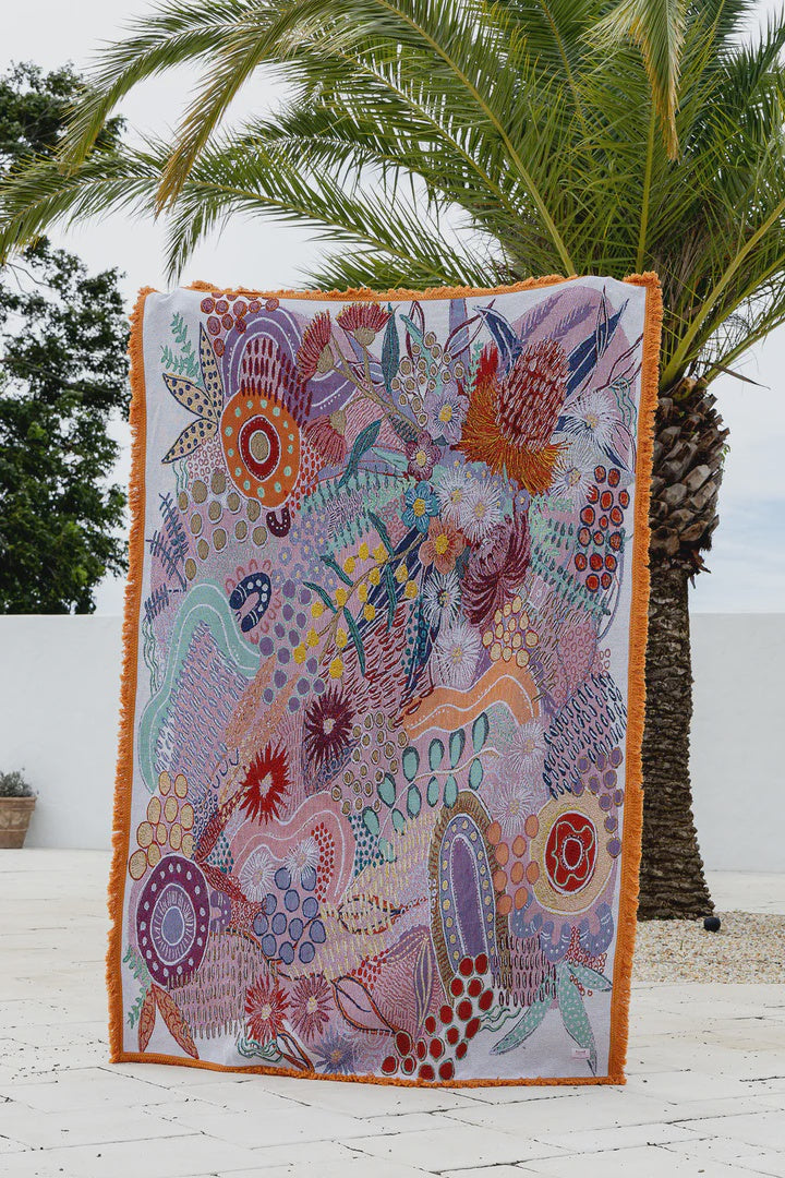 Colorful patterned blanket on a wooden floor with palm trees in the background