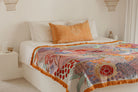 Bed with a colorful patterned throw blanket and an orange pillow.