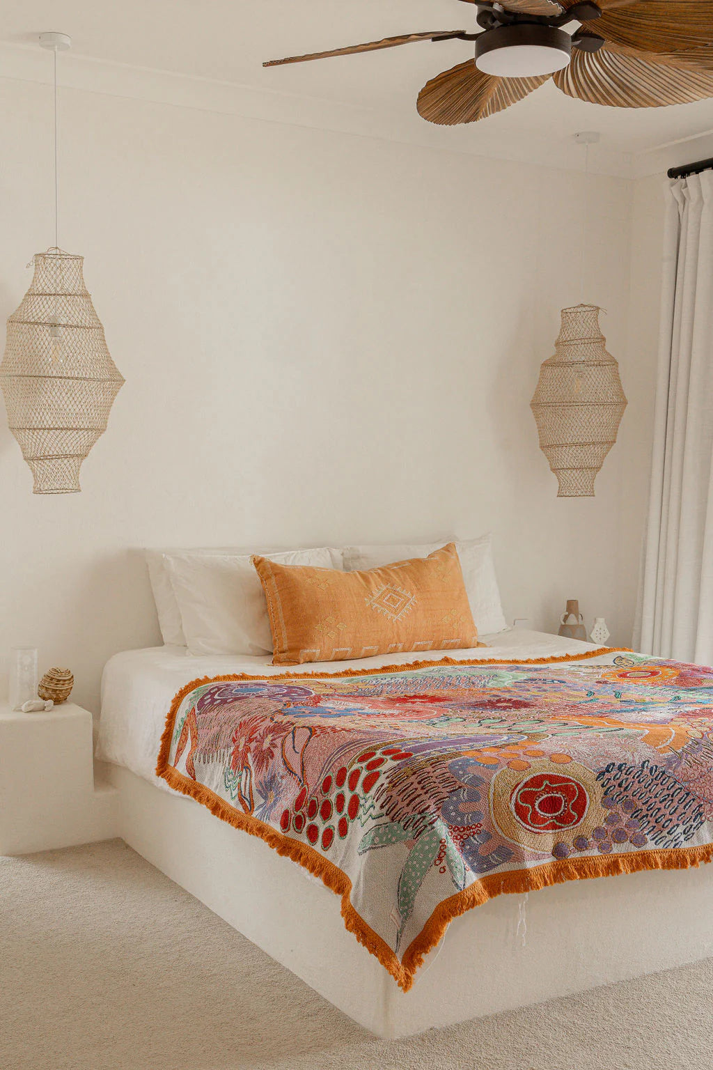 Bedroom with a colorful patterned blanket on a bed, surrounded by decorative lamps and a ceiling fan.