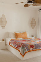 Bedroom with a colorful patterned blanket on a bed, surrounded by decorative lamps and a ceiling fan.