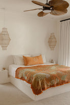 Bedroom with a bed featuring an orange and green blanket, white pillows, and decorative lamps.
