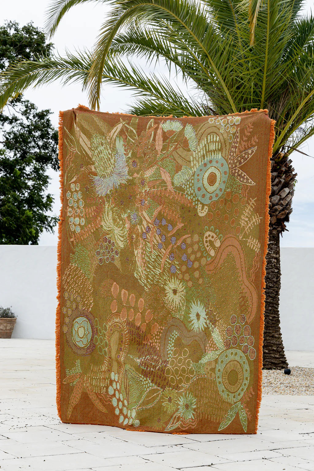 Decorative blanket with intricate patterns on a white surface with palm trees in the background
