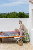 Woman sitting at a table with a colorful tablecloth in an outdoor setting.