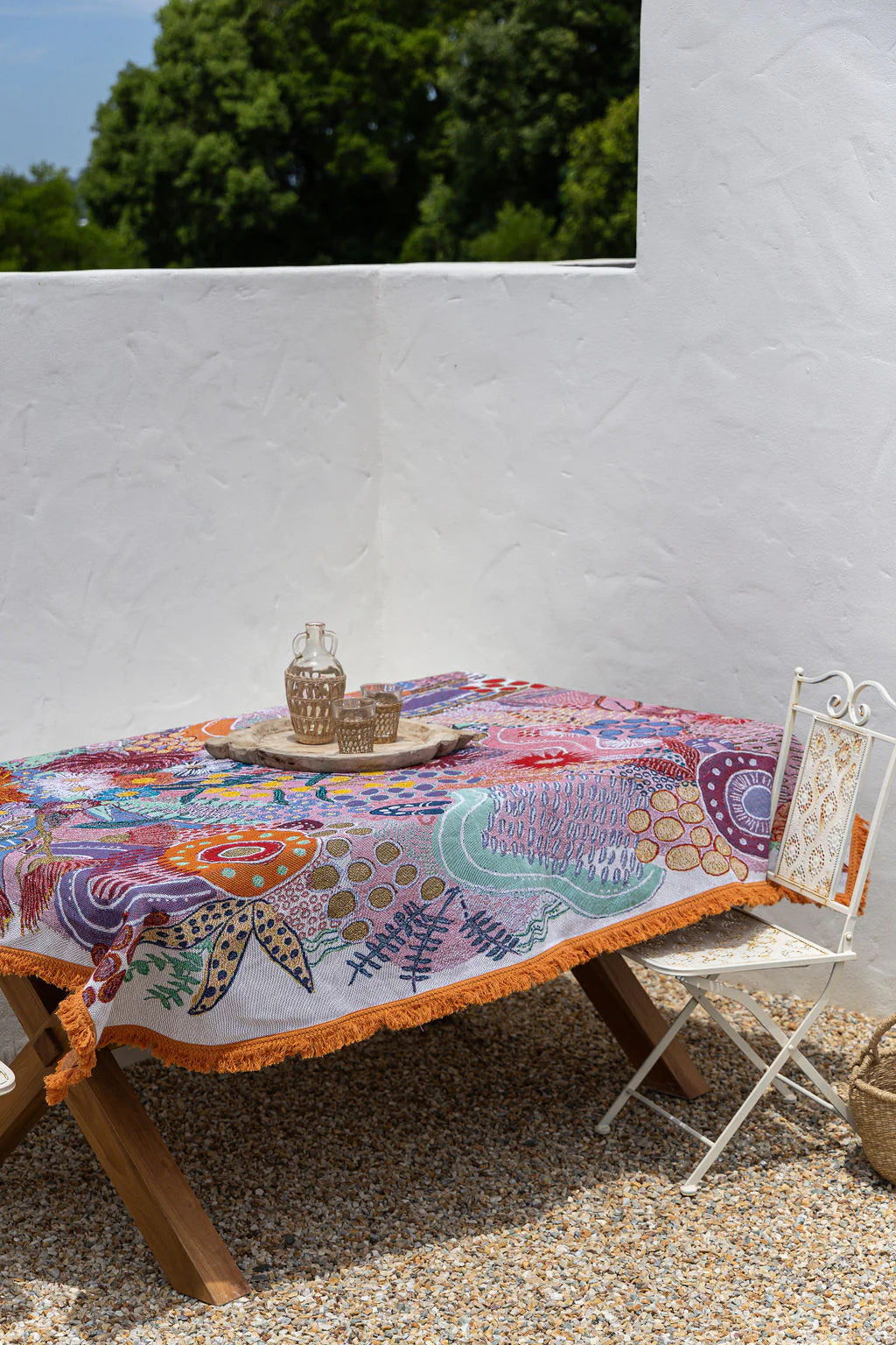 Colorful embroidered tablecloth on a wooden table with a white wall and greenery in the background